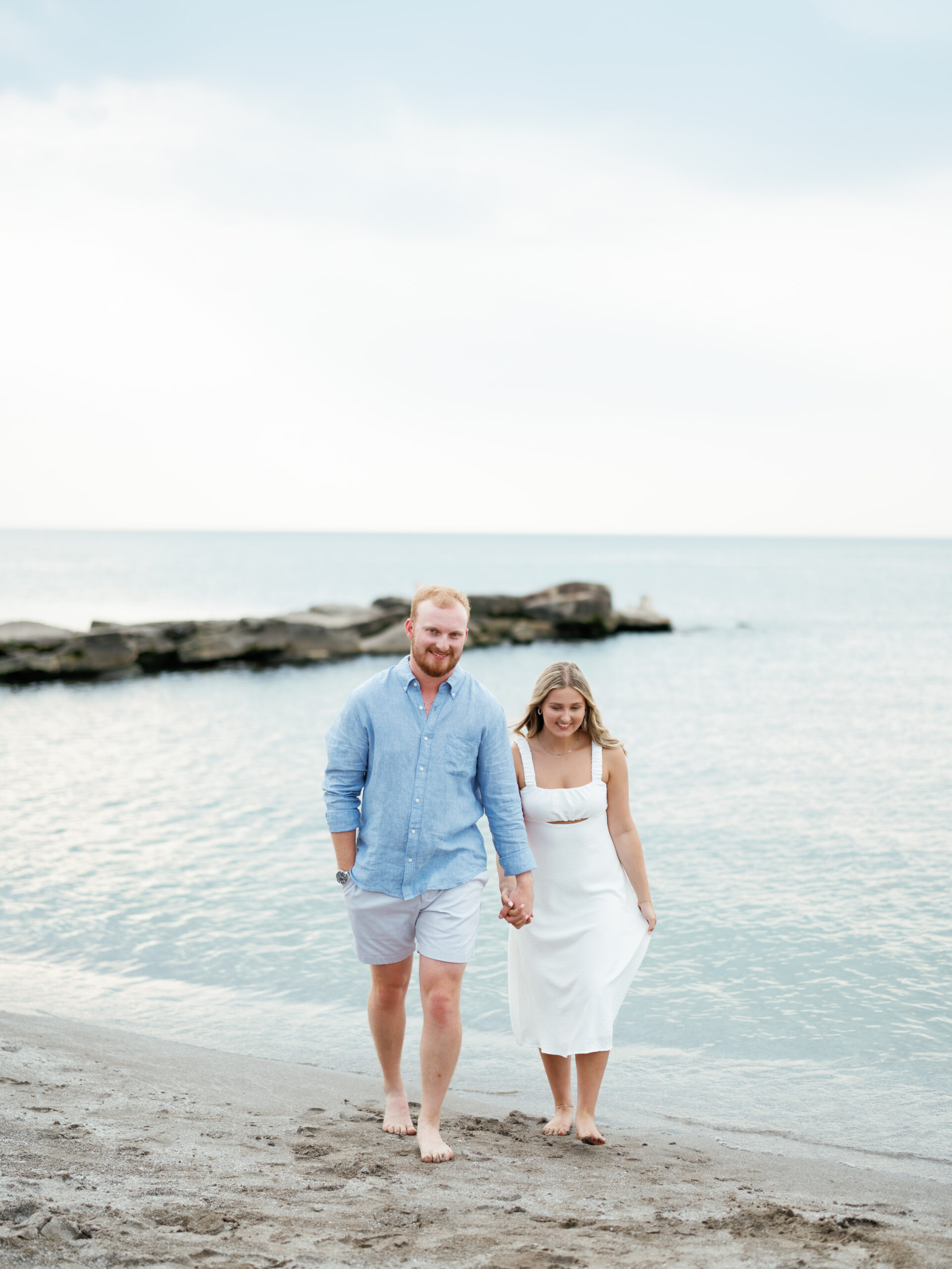 Couple walks barefoot along the shoreline during their Cleveland engagement session at Edgewater Beach.
