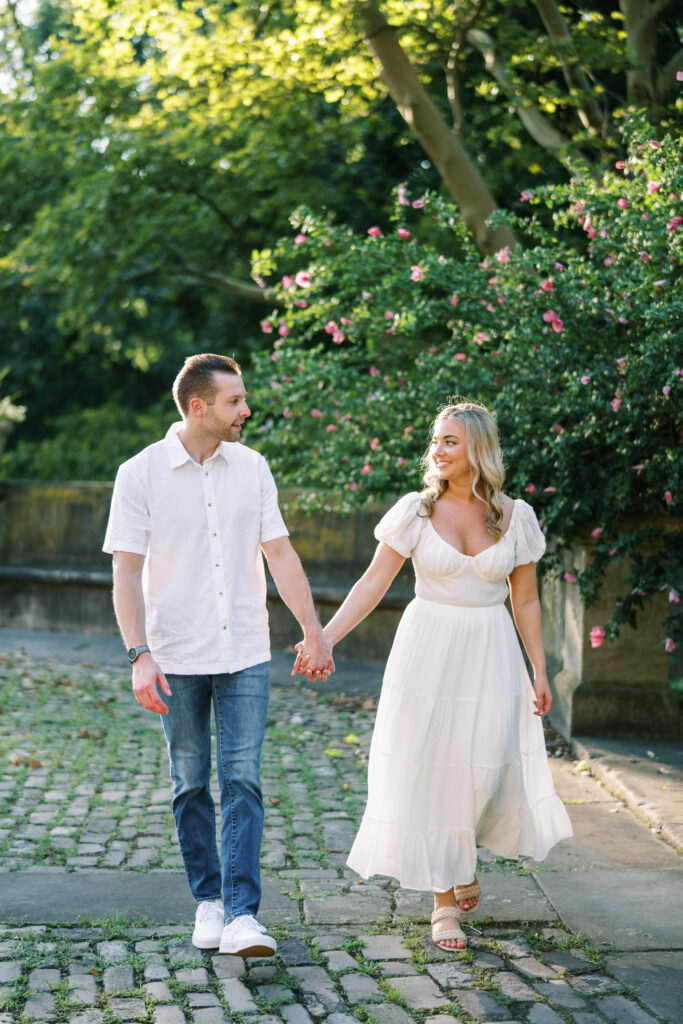 Couple walking hand in hand through a flower-lined path during a summer engagement session at The Cultural Gardens in Cleveland.