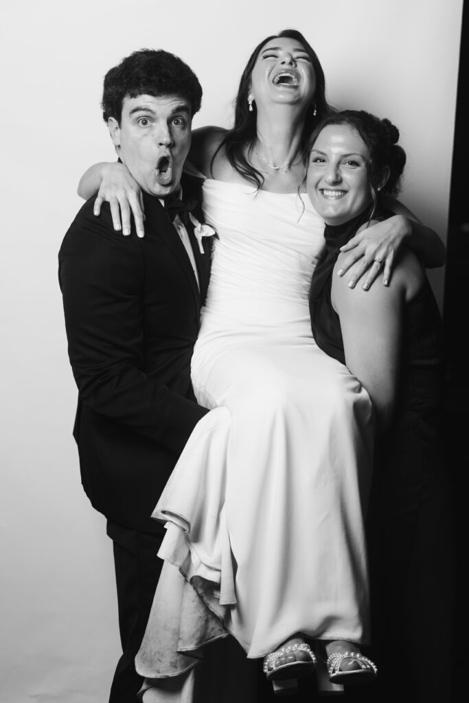 Bride laughing while being lifted by groom and bridesmaid.